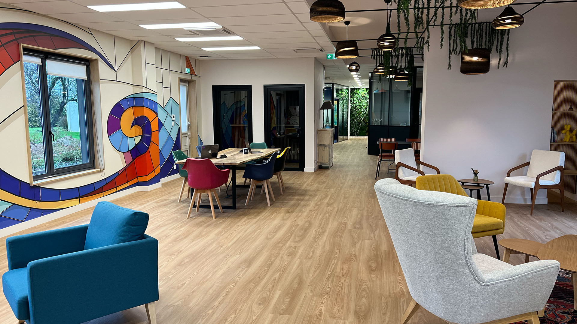 Espace de vie convivial avec fresque colorée reprenant la mosaïque du patio dans la pièce commune principale de La Passerelle Coworking, lieu de travail et lieu de vie accueillant