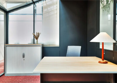 Intérieur d’un bureau individuel de 15m², équipé d’un grand bureau en bois clair, d’une chaise ergonomique et d’une lampe design, avec rangements et cloison vitrée.