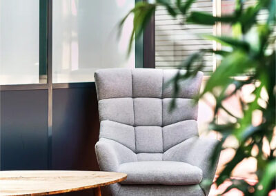 Fauteuil gris capitonné design accompagné d’une table basse en bois, installé sur un tapis oriental coloré, entouré de plantes vertes.