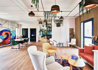 Grand espace de vie avec table en bois massif, chaises colorées, suspensions lumineuses design et cuisine ouverte, ambiance chaleureuse et végétalisée.