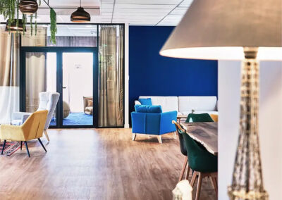 Grand espace commun avec fauteuils design, canapé rouge, luminaires suspendus et touches végétales décoratives.