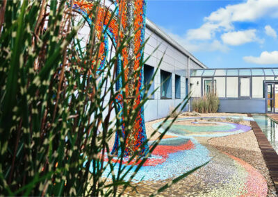 Patio extérieur avec fresque artistique colorée, allée en bois et plantes décoratives sous ciel bleu.