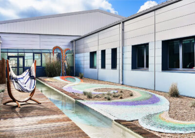 Patio aménagé avec hamac suspendu, allée en bois, bassin d’eau et mosaïque colorée au sol.