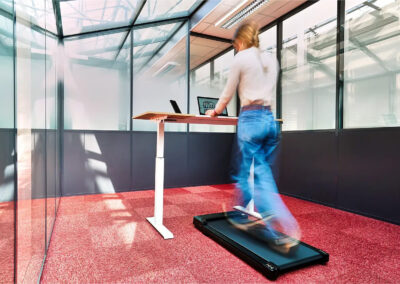 Bureau lumineux équipé d’un poste assis-debout et d’un tapis de marche, permettant de travailler en mouvement dans un environnement vitré moderne.