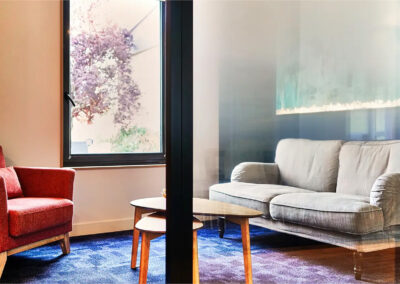 Espace de réunion Amélie avec fauteuil rouge, canapé gris et tables basses en bois, décor chaleureux et ambiance intimiste.