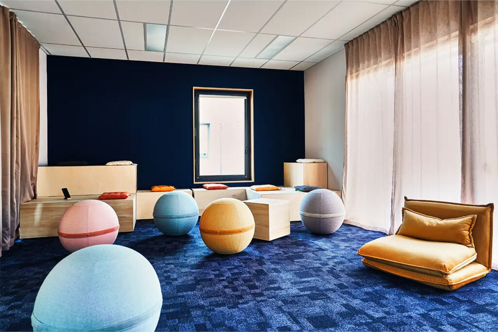 Salle Créa Inès avec coussins au sol, assises modulables, ballons colorés et décor mural artistique, conçue pour stimuler la créativité.