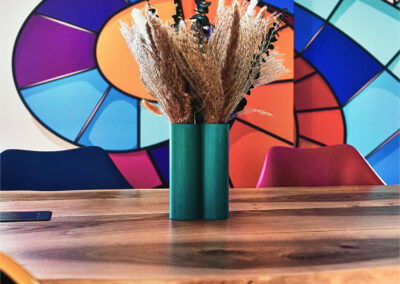 Grande table en bois clair entourée de chaises design, située dans le grand salon lumineux de La Passerelle.