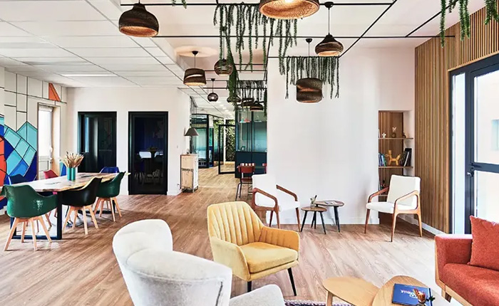 Grand espace commun avec fauteuils design, canapé rouge, luminaires suspendus et touches végétales décoratives.